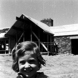 Smiling young girl in sweater outdoors near rustic buildings.