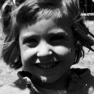 Smiling young girl in sweater outdoors near rustic buildings.