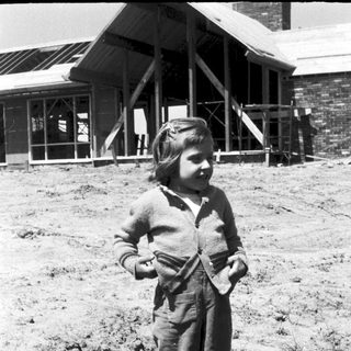 Young girl in overalls posing outdoors near building.