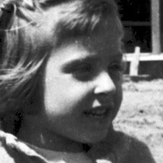 Young girl in overalls posing outdoors near building.