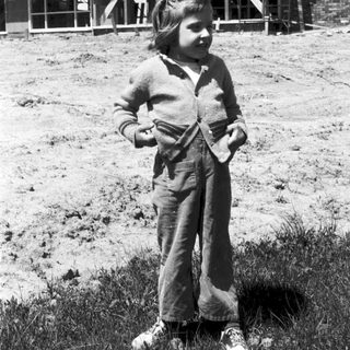 Young girl in overalls posing outdoors near building.