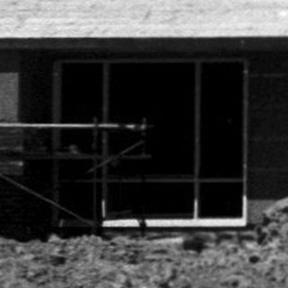 Mid-century modern house under construction on grassy hill.