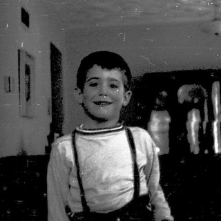 Young boy smiling indoors with suspenders.