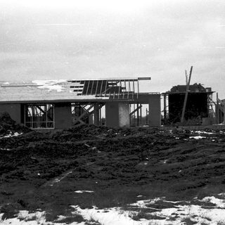 Mid-century modern house under construction on snowy ground.