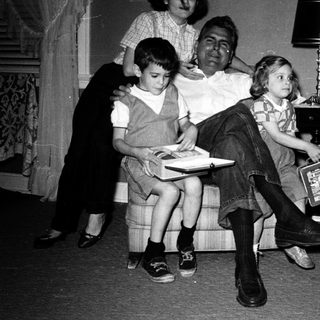Family posing indoors with vintage luggage and books.