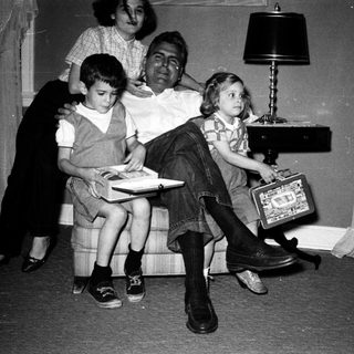Family posing indoors with vintage luggage and books.