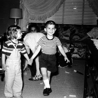 Two children playing indoors with adult supervising.