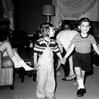 Two children playing indoors with adult supervising.