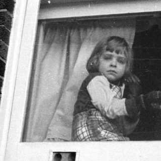 Child peering out of a window frame.