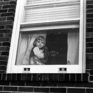 Child peering out of a window frame.