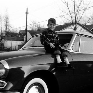 Young boy sitting on vintage car hood.