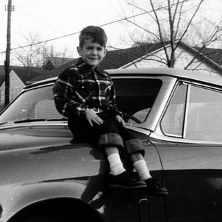 Young boy sitting on vintage car hood.
