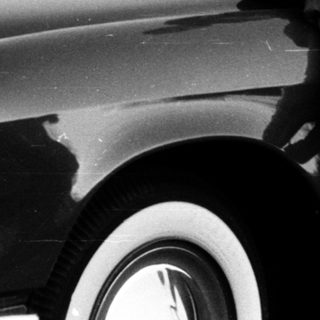 Young boy sitting on vintage car hood.