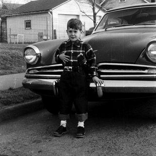 Young boy sitting on vintage car hood.