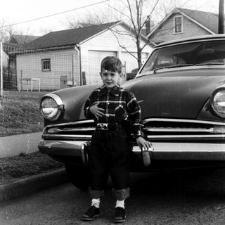 Young boy sitting on vintage car hood.