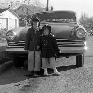 Two children standing before a vintage car.