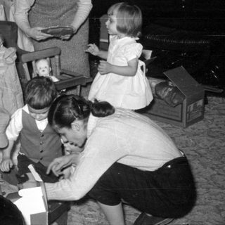 Family gathering around a Christmas tree opening gifts.