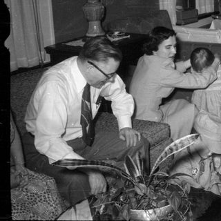 Family gathering around a Christmas tree opening gifts.