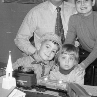 Family posing with model trains and Christmas tree.