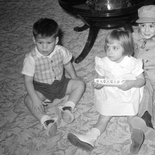 Four children sitting on a carpet indoors.