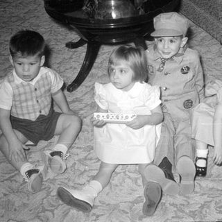 Four children sitting on a carpet indoors.