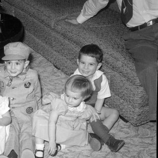 Four children sitting on a carpet indoors.
