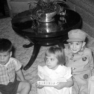 Four children sitting on a carpet indoors.