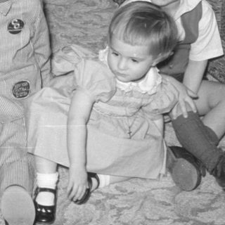 Four children sitting on a carpet indoors.