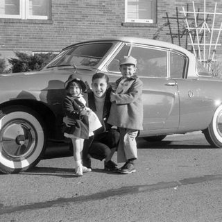 Man and two children posing by a vintage coupe.