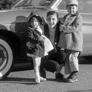Man and two children posing by a vintage coupe.