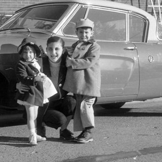 Man and two children posing by a vintage coupe.