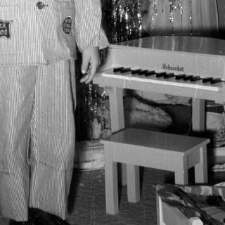 Child in striped suit standing by Christmas tree.
