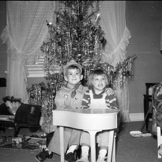 Two children posing by a decorated Christmas tree.