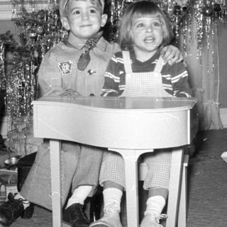 Two children posing by a decorated Christmas tree.