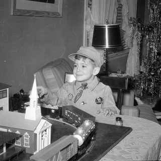Boy in conductor outfit with model train set.