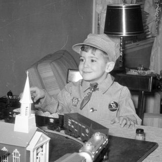 Boy in conductor outfit with model train set.