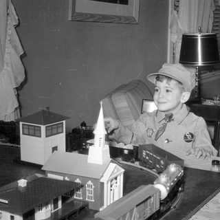 Boy in conductor outfit with model train set.