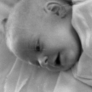 Infant lying on a pillow and patterned quilt.