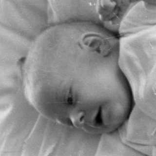 Infant lying on a pillow and patterned quilt.