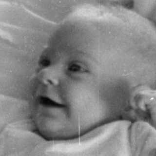 Infant lying on a pillow on patterned bedding.