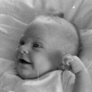 Infant lying on a pillow on patterned bedding.