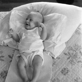 Infant lying on a pillow on patterned bedding.