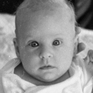 Infant on a bed with a woman and desk.
