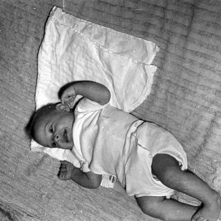 Infant lying on a striped blanket and white cloth.