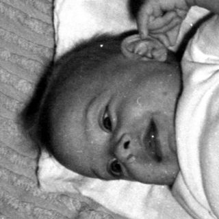 Infant lying on a striped blanket and white cloth.
