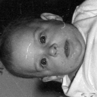 Infant in a bodysuit lying on a bed.