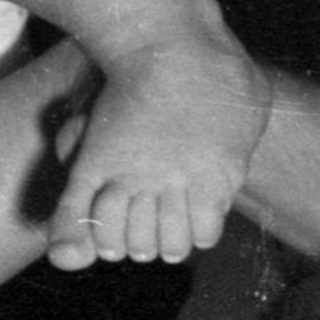 Infant in a bodysuit lying on a bed.