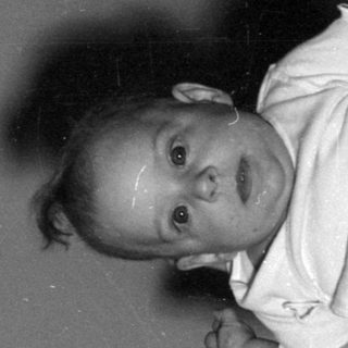 Infant in a bodysuit lying on a bed.