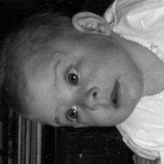 Infant lying on a textured blanket in a room.