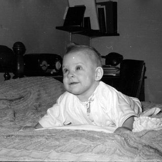 Baby in white clothing lying on a blanket.
